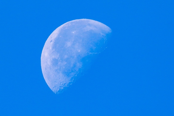 A Shot of the moon in daytime showing crater detail against a blue sky